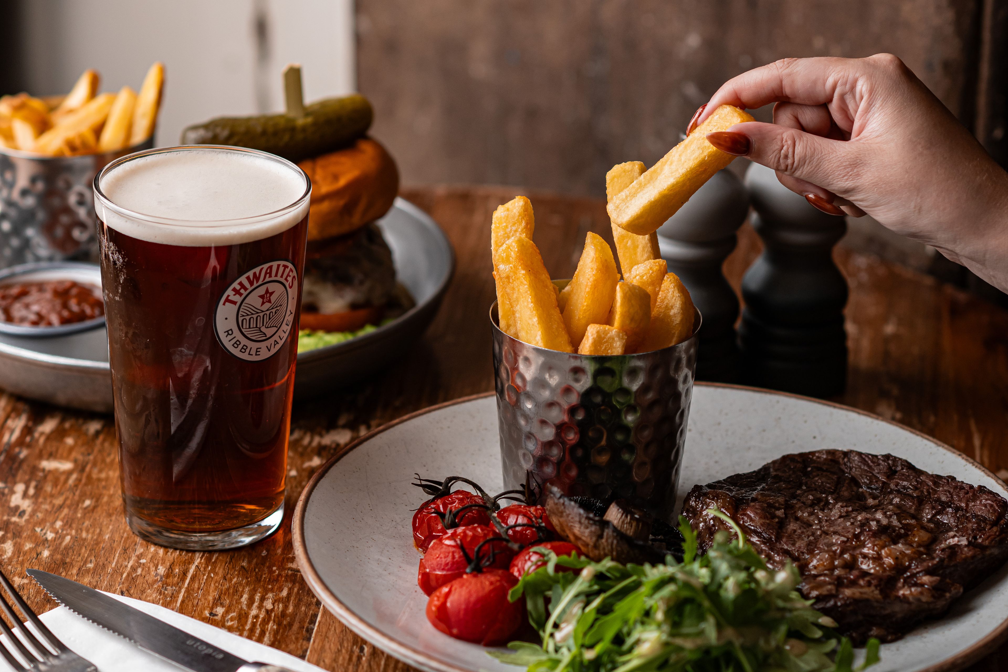 person picking up a chip from steak and chips dish