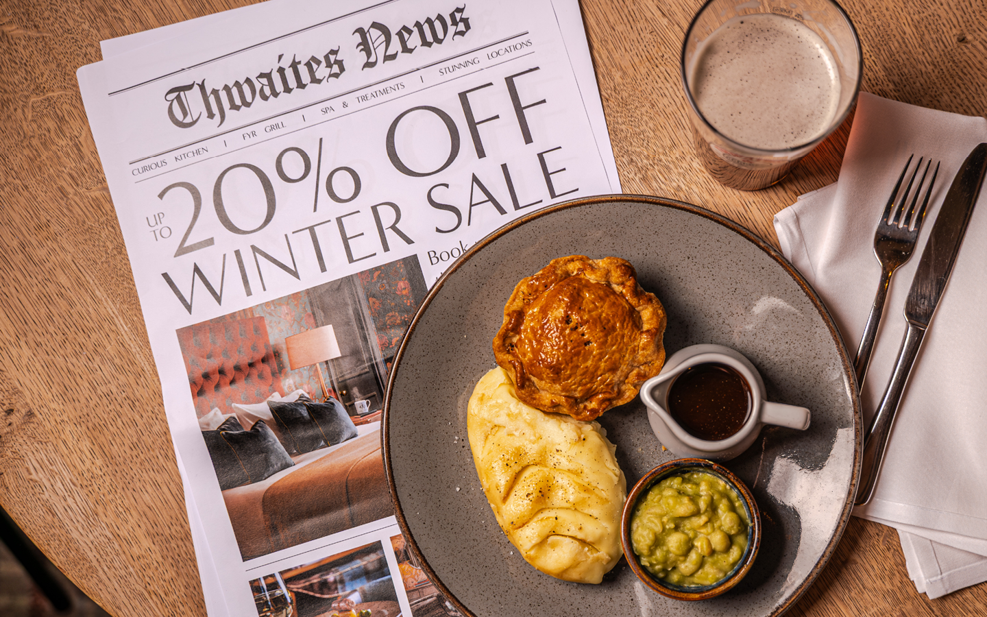 "up to 20% off this winter" newspaper with pie and a pint flat lay on a pub table